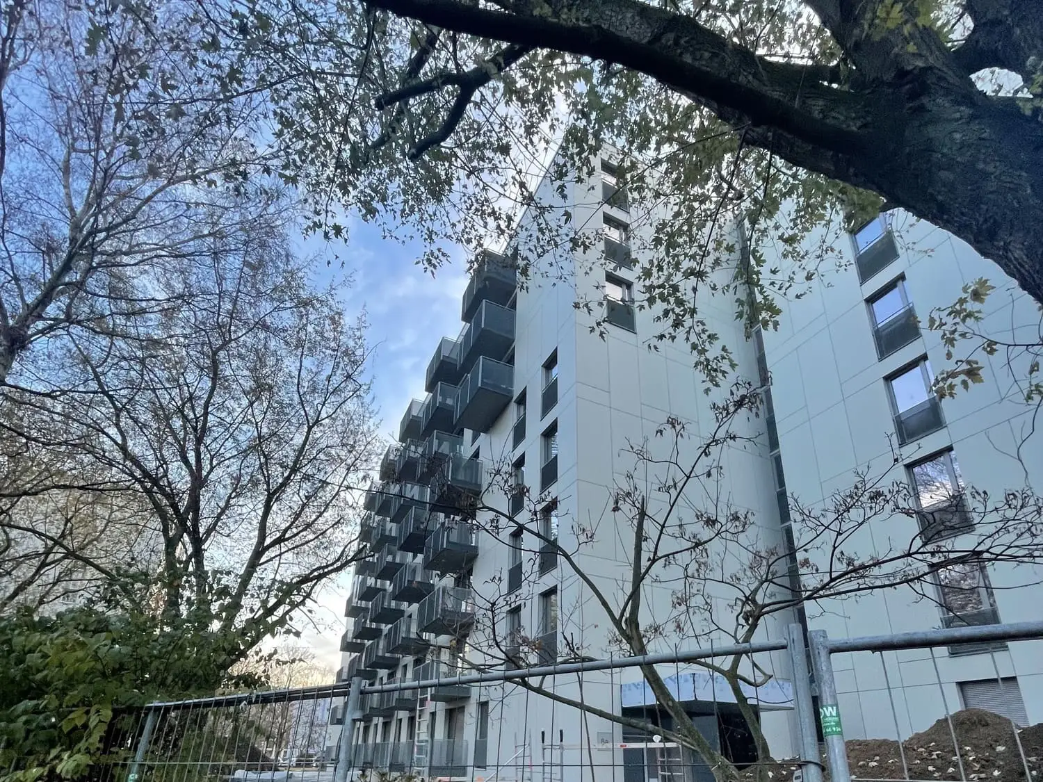 neu gebauter Wohnblock hinter Bauzaun und Bäumen